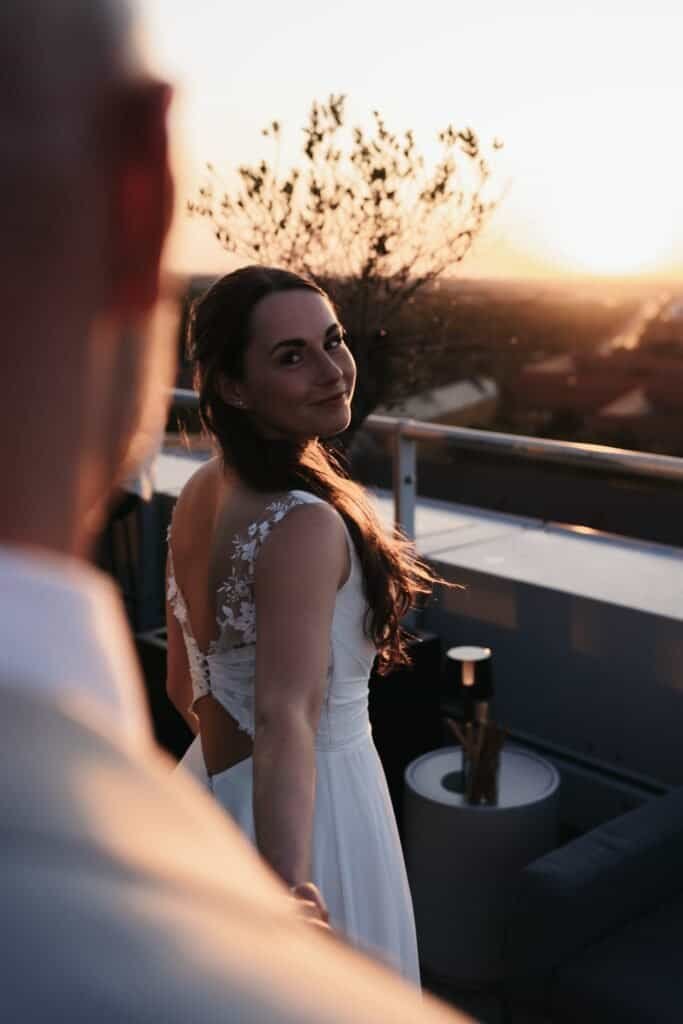Braut schaut verträumt während des Sonnenuntergangs auf der Dachterrasse, emotionaler Moment, candid, editorial Stil.