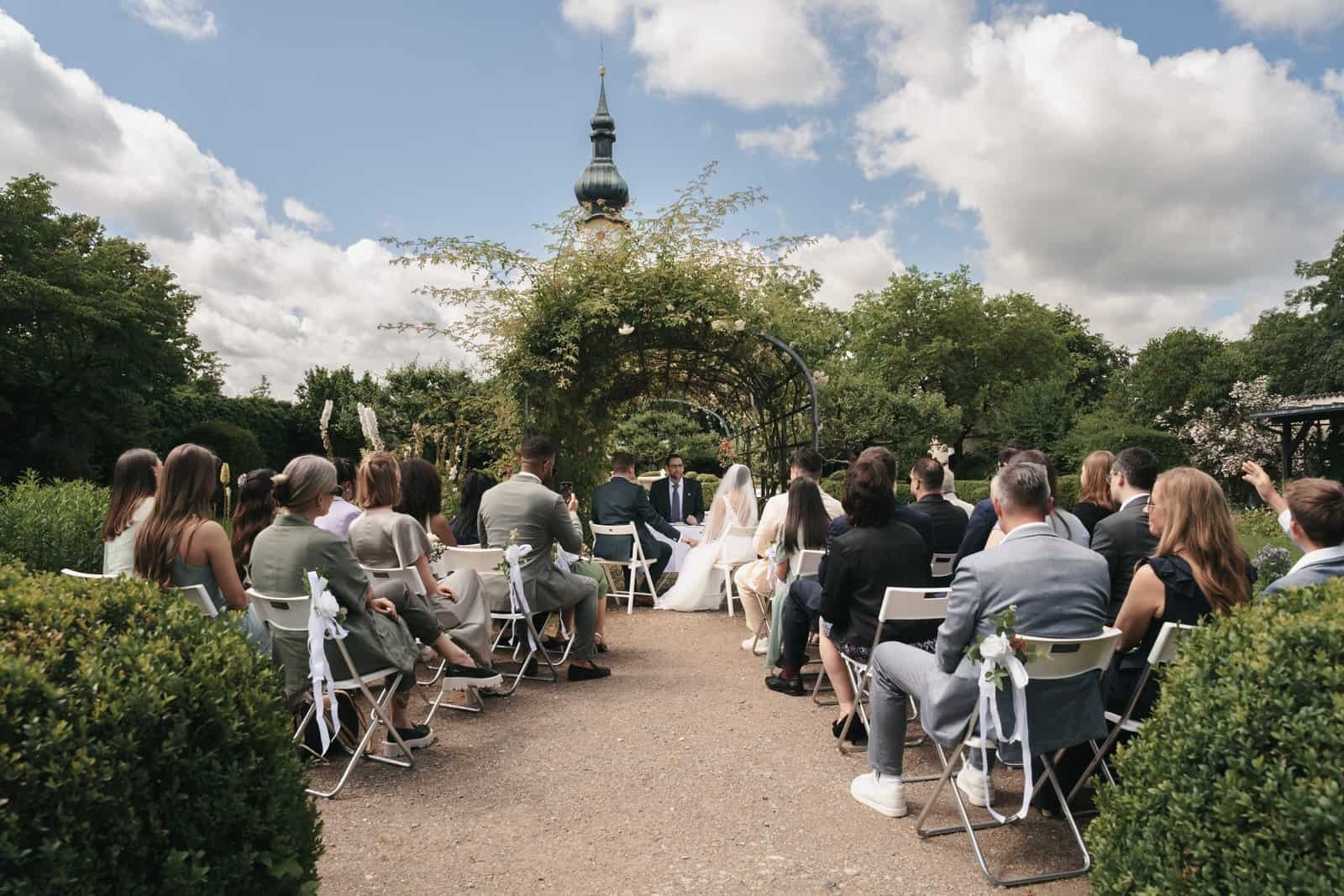 Weitläufige, elegante Trauung im sonnigen Schlossgarten Starnberg unter blauem Himmel. Hochzeitsreportage im Premium-Segment, fotografiert im Raum München.