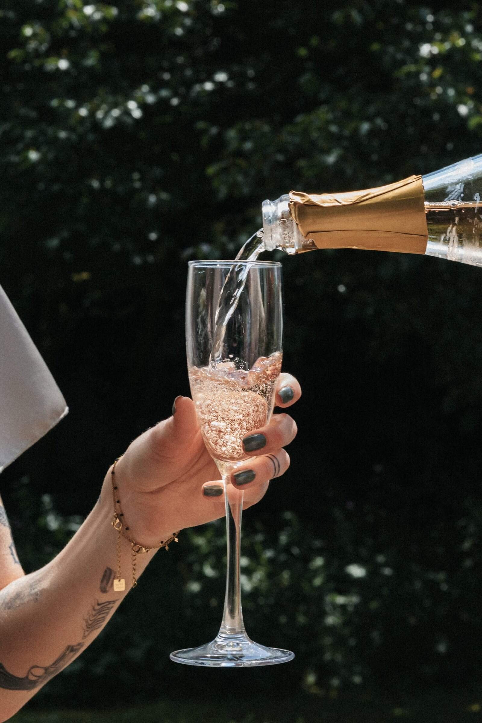 Detailaufnahme beim Sektempfang: Champagner wird an einem sonnigen Tag in ein Glas eingeschenkt, Hochzeitsreportage im Schlossgarten Starnberg.