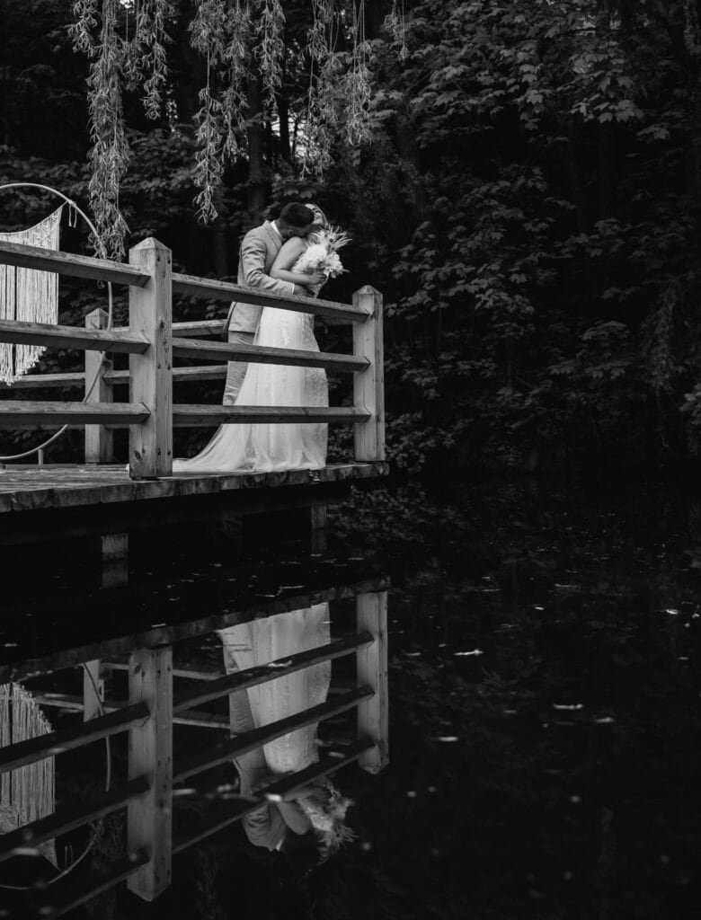 Ein romantisches Hochzeitsfoto eines Paares, das sich auf einer Holzbrücke am Wasser in München küsst, aufgenommen von Hochzeitsfotograf München.