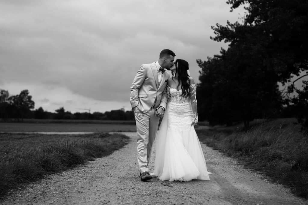 Ein Brautpaar in eleganter Hochzeitskleidung auf einem ländlichen Weg, umgeben von Natur, fotografiert von Hochzeitsfotograf München.