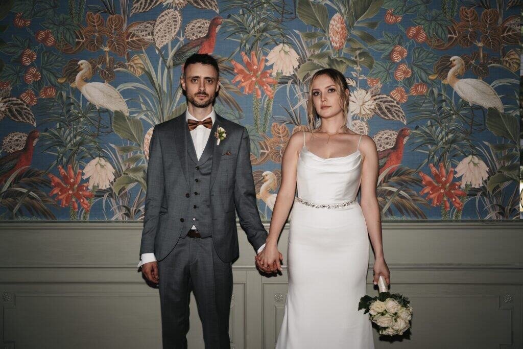 Ein Brautpaar hält Händchen vor einer bunten Dschungel-Wand, Hochzeitsfotograf München.