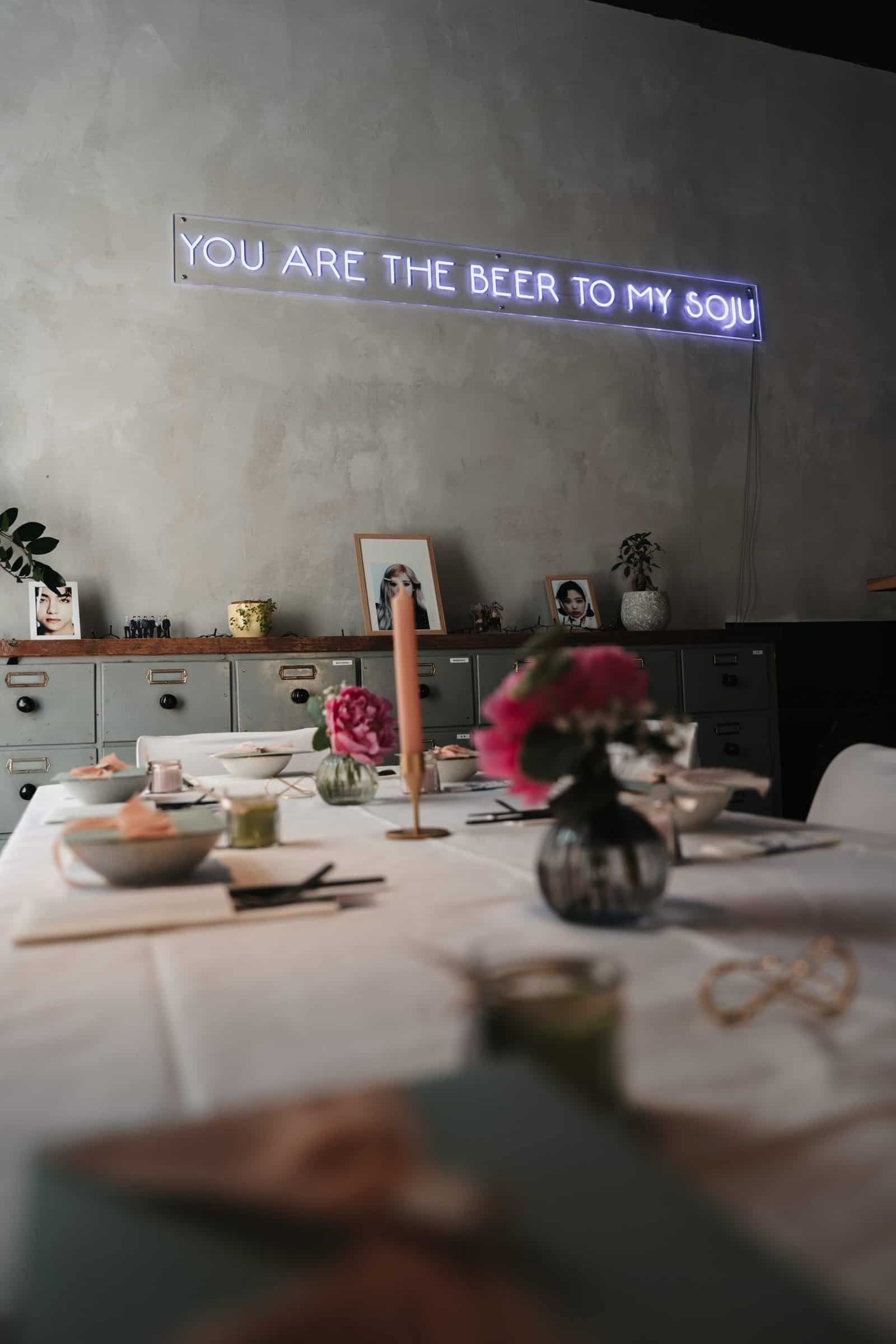 Stylisches Neon-Schild mit der Aufschrift 'You are the beer to my soju' über der festlich gedeckten Tafel in der Hochzeitslocation Anju in München.