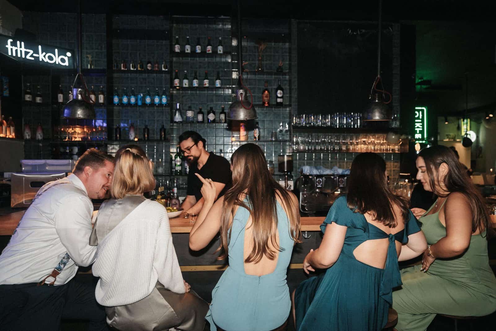 Ausgelassene Hochzeitsgesellschaft feiert an der beleuchteten Bar der Location Anju in München.